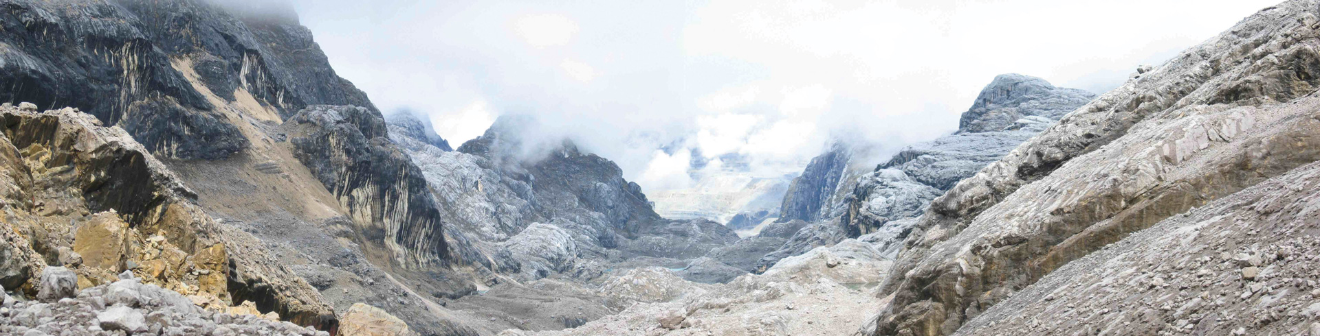 An image of a rocky and barren mountain top, partially covered in clouds.